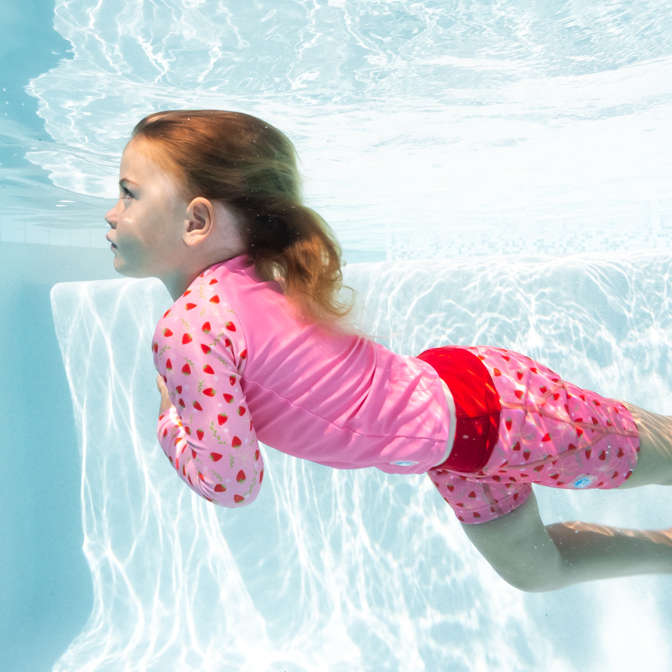 little girl swimming underwater wearing the long sleeve rash top and matching splash jammer duo swimwear