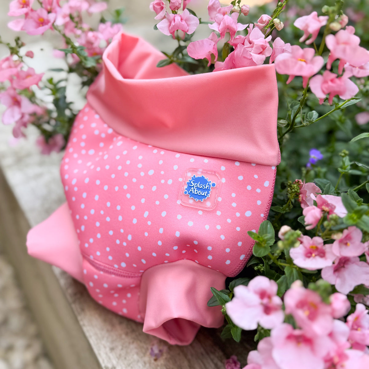 Pink swim diaper with white polka dots and a splash about logo, surrounded by pink flowers.