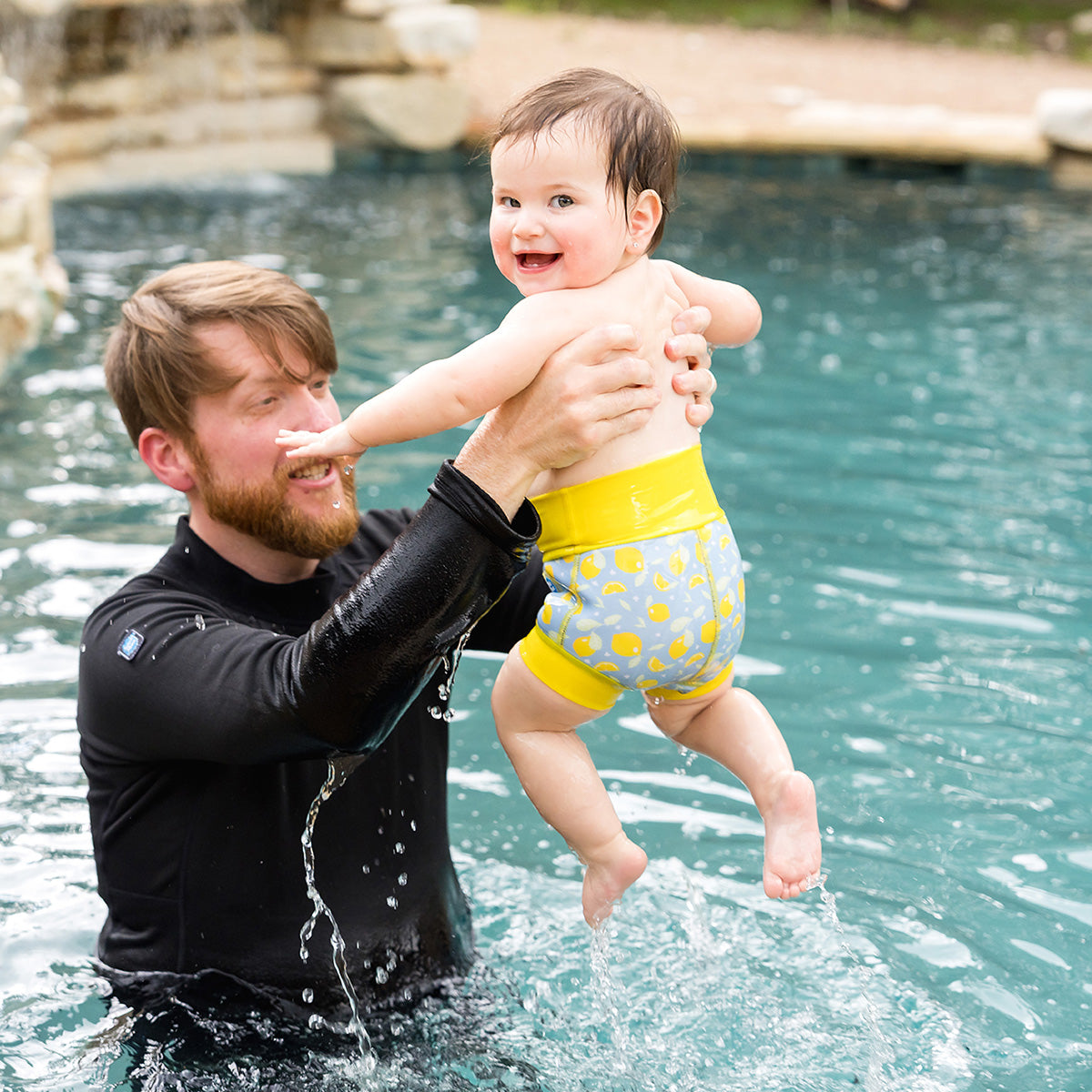 baby in the pool with dad swimming wearing the happy nappy swim diaper lemon print yellow and blue
