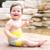 baby sat near the water wearing a lemon print happy nappy swim diaper
