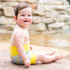 baby sitting next to the water wearing the lemon print swim diaper 