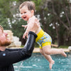 man lifting baby in the pool wearing the happy nappy lemon print swim diaper