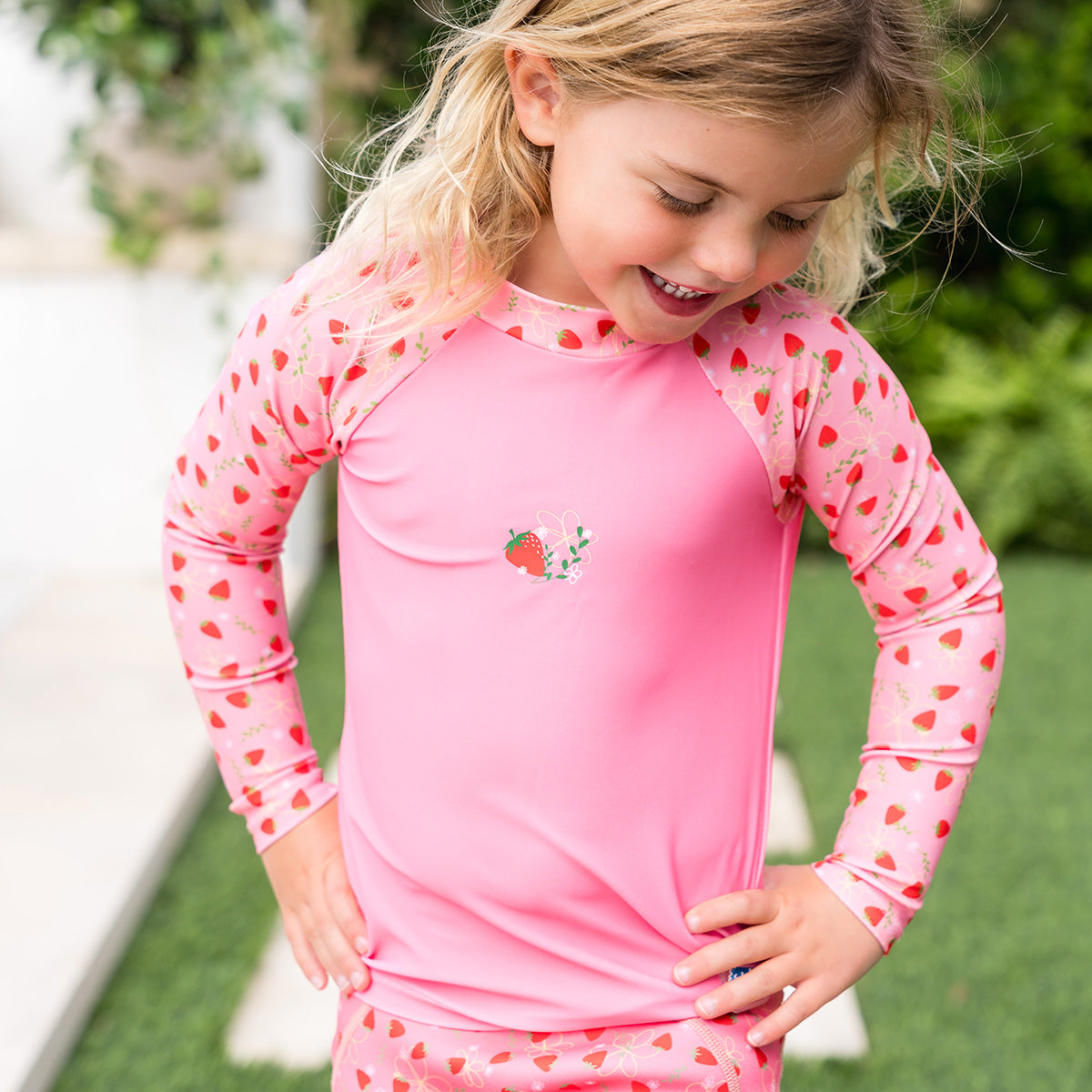 little girl stood in a garden wearing the strawberry long sleeve rash top 