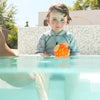 little boy in the swimming pol wearing shorty wetsuit playful otter and holding orange pufferfish toy 